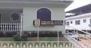 Fachada de delegacia com brasão e letreiro 'Polícia Civil' atrás de grade