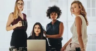 Grupo de mulheres reunidas em escritório em torno de mesa com notebook