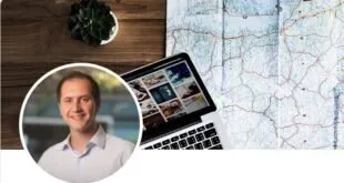 Notebook aberto sobre mapa impresso ao lado de xícara e planta, com retrato circular de homem sorridente