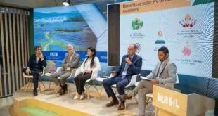 Pessoas sentadas em painel de debate sobre palco de evento com telão ao fundo