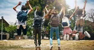 Grupo de jovens com mochilas pulando de costas em parque ensolarado
