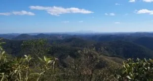 Vista de montanhas cobertas por mata sob céu azul com poucas nuvens