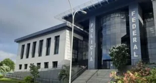 Fachada de prédio público moderno com vidros escuros, escadaria e jardim na entrada