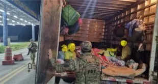 Agente da Polícia Rodoviária Federal diante de baú de caminhão com pessoas e bagagens