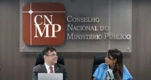 Duas pessoas sentadas à mesa diante de painel do Conselho Nacional do Ministério Público