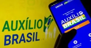 Celular exibindo aplicativo diante de painel amarelo com a marca Auxílio Brasil