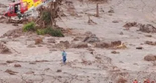Helicóptero de resgate sobrevoando área tomada por lama com equipes em busca
