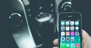 Mão segurando celular dentro de carro ao lado do câmbio e do painel