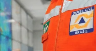 Detalhe de uniforme laranja com bandeira do Brasil e brasão costurados no braço