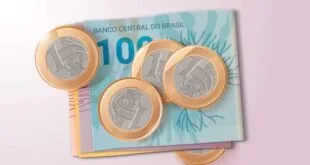 Moedas de um real sobre cédula de cem reais em fundo rosa
