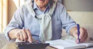 Mulher idosa usando calculadora ao lado de papéis sobre a mesa