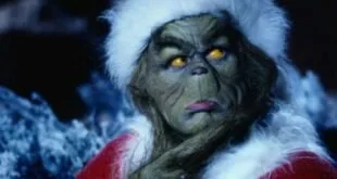 Personagem de rosto verde vestido de Papai Noel com expressão irritada