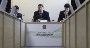 Autoridades em bancada de coletiva diante de painel do Ministério da Infraestrutura