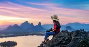 Viajante sentado em rocha contemplando lago e montanhas ao pôr do sol
