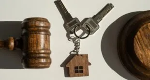 Martelo de juiz ao lado de chaves com chaveiro em forma de casa sobre fundo claro