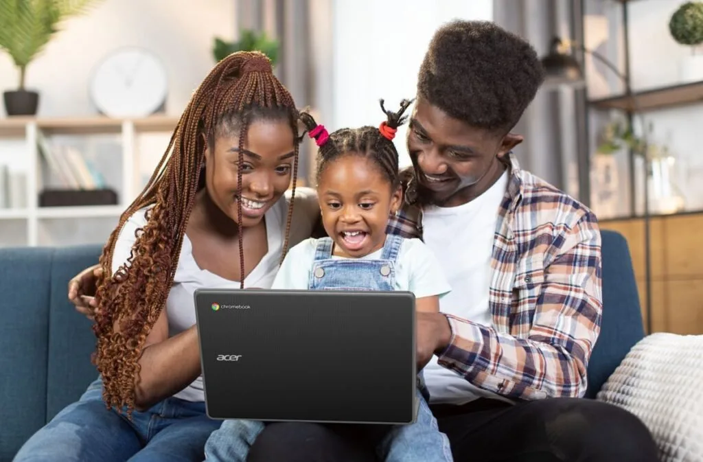 Casal e criança sorrindo no sofá diante da tela de um notebook Acer aberto