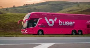 Ônibus rodoviário rosa em movimento em rodovia com o logotipo 'bus' na lateral