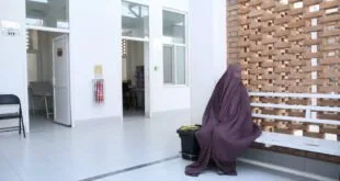 Mulher de burca roxa sentada no chão encostada em parede de tijolos em corredor