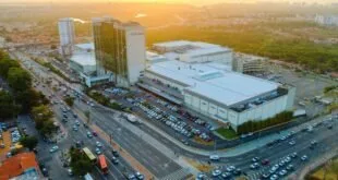 Vista aérea de complexo de shopping center com estacionamento cheio e avenida movimentada ao pôr do sol
