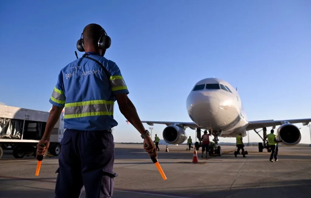 Agente de pátio com colete refletivo e bastões sinalizadores diante de avião estacionado