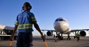 Agente de pátio com colete refletivo e bastões sinalizadores diante de avião estacionado