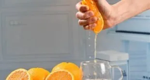 Mão espremendo metade de laranja sobre jarra, imagem ilustrativa sobre contas laranjas