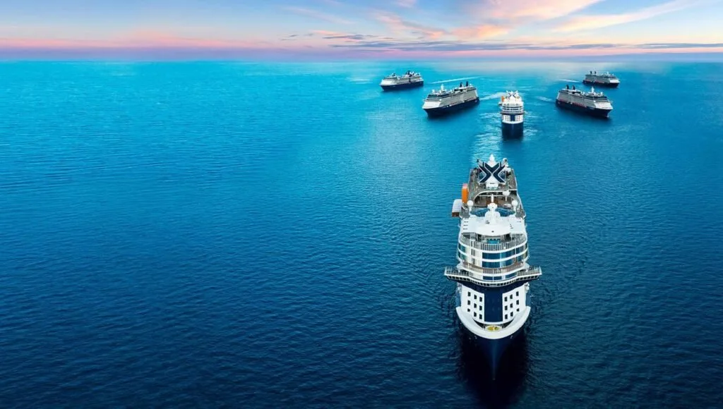 Vista aérea de navio de cruzeiro navegando em mar azul com outras embarcações ao fundo no fim da tarde