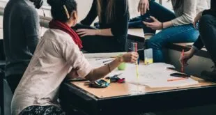Jovens reunidos em torno de mesa com folhas de papel e canetas coloridas durante atividade em grupo