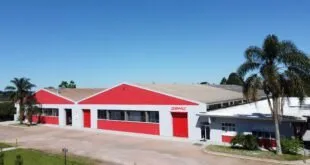 Galpão industrial vermelho e branco com o letreiro 'GEMÜ' na fachada sob céu azul