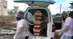 Pessoas de máscara ao lado de caixões de madeira empilhados em veículo branco
