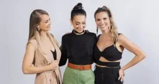 Três mulheres posando juntas e sorrindo diante de fundo branco de estúdio