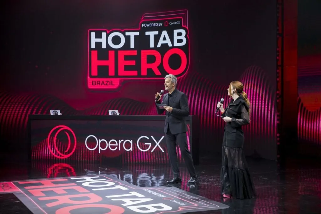 Dois apresentadores no palco diante de telão com os letreiros 'HOT TAB HERO' e 'Opera GX'