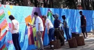 Grupo de pessoas pintando muro azul ao ar livre com baldes de tinta no chão