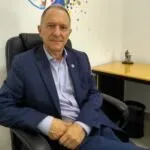 Homem de terno azul sentado em cadeira de escritório diante de parede com pintura colorida