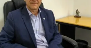 Homem de terno azul sentado em cadeira de escritório diante de parede com pintura colorida