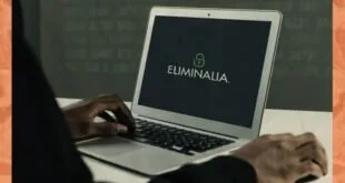 Pessoa digitando em notebook com o logotipo 'ELIMINALIA' na tela, em ambiente escuro