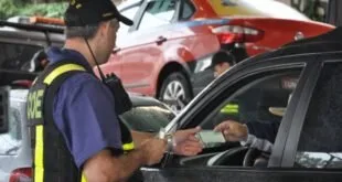 Agente de uniforme abordando motorista pela janela do carro em fila de trânsito