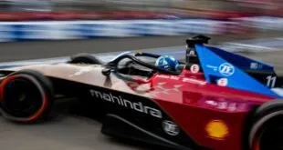 Carro de corrida elétrico vermelho e azul em alta velocidade na pista, com a marca Mahindra na lateral