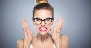 Mulher de óculos com expressão de irritação e mãos erguidas sobre fundo cinza, imagem ilustrativa