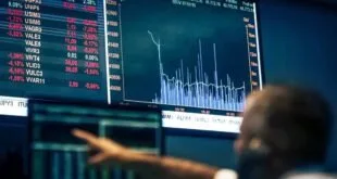 Homem de costas diante de painéis eletrônicos com cotações e gráficos da bolsa de valores