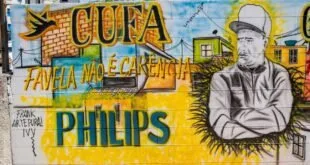 Muro grafitado em amarelo e azul com as inscrições 'CUFA' e 'Philips' e o rosto de um homem pintado
