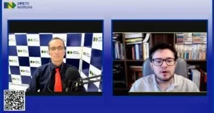 Captura de tela de entrevista em vídeo com apresentador ao microfone e convidado diante de estante de livros