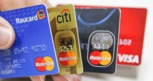 Mão segurando três cartões de crédito em leque, com bandeiras e números em relevo