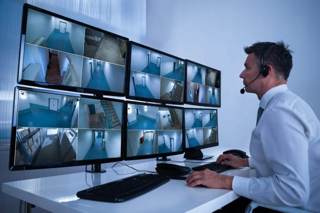 Homem com fone de ouvido observando seis monitores com imagens de câmeras de segurança