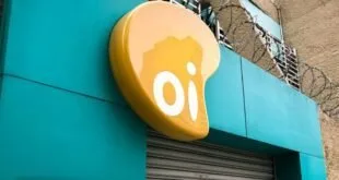 Placa amarela com o logotipo da Oi na fachada de uma loja com porta de aço fechada