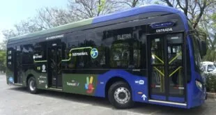 Ônibus elétrico azul e verde com a marca Transcol na lateral, estacionado sob árvores