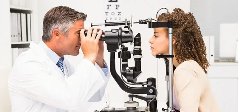 Oftalmologista examinando os olhos de uma paciente em aparelho de consultório, com tabela de letras ao fundo