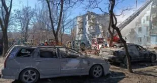 Carro destruído em rua coberta de escombros diante de prédio residencial danificado