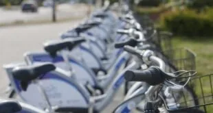 Fileira de bicicletas brancas e azuis estacionadas em estação de aluguel à beira da rua