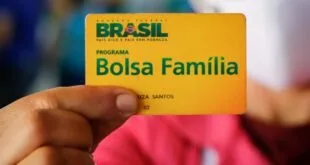 Mão segurando cartão amarelo do programa Bolsa Família com o brasão do Brasil